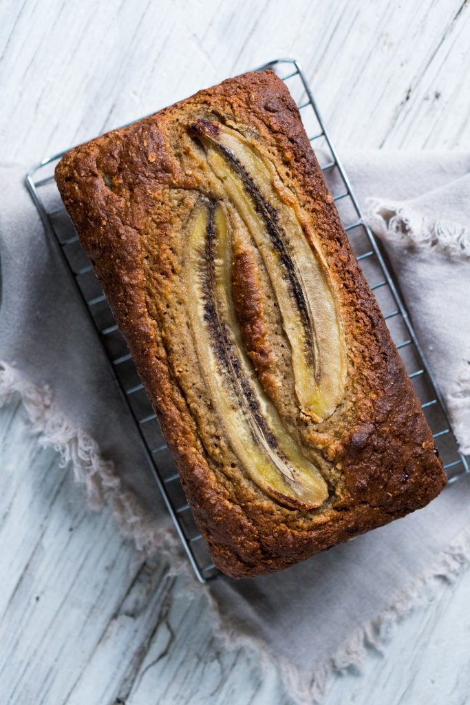 banana bread, with split bananas on an unsliced loaf on a cooling rack 