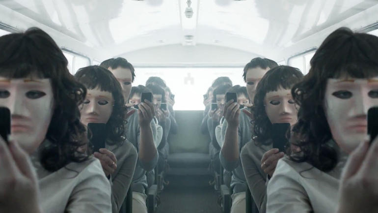 Black Mirror show, people in identical masks & wigs holding phones in a bus 
