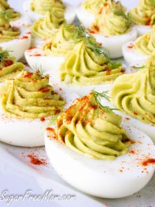 a plate of avocado deviled eggs topped with dill and paprika