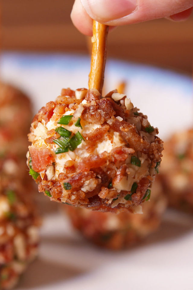 a loaded cheese ball covered in bacon held by a pretzel stick