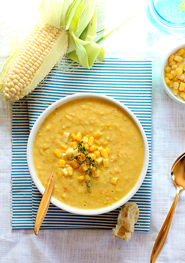 corn chowder soup in a white bowl over a striped towel next to corn on the cob